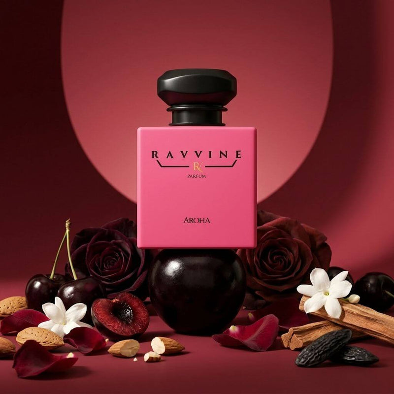 A perfume bottle labeled RAVVINE PARFUM and AROHA, with a bright pink rectangular bottle and a glossy black rounded cap, styled with dark red roses, cherries, white flowers, cinnamon, and nuts on a deep red background. Inspired by Tom ford Lost Cherry