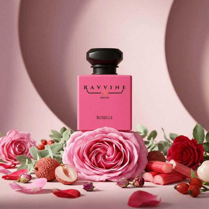 A pink rectangular perfume bottle labeled 'RAVIVNE ROSELLE' stands centered among pink and red roses, petals, and botanical elements on a soft pink studio background. Inspired by PDM Delina